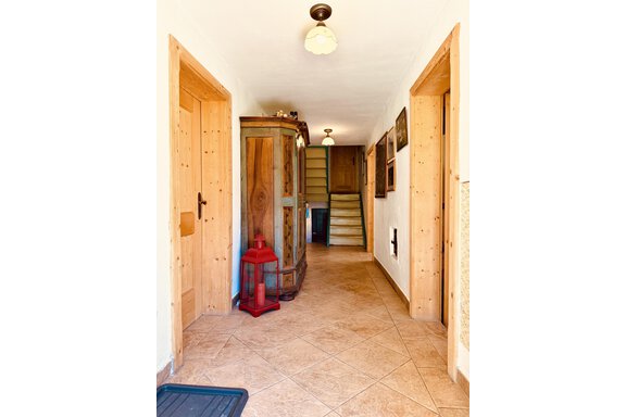 A bright hallway with wooden details and a staircase. To the left stands a decorative cabinet and a red light. - Haus Freistabl - Vent