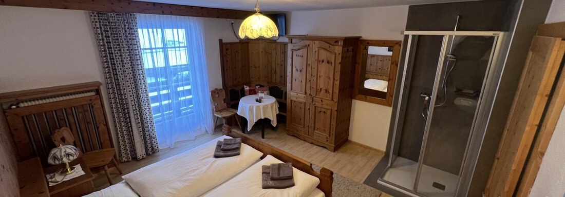 A cozy bedroom with a double bed and wooden furniture. There is a dining table and a shower room in the room. - Haus Reinstadler - Vent