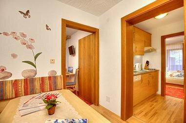 A bright and inviting apartment with a kitchen area and a dining space. The room is tastefully decorated with a flower wall and wooden details. - Haus Weisskogelblick - Vent