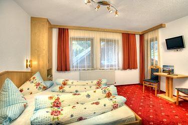 Zimmer A cozy room with two beds, colorful bedding, and wooden paneling. The room has windows with curtains and a small table with a chair. - Haus Weisskogelblick - Vent