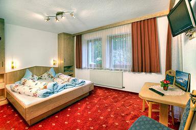 A cozy bedroom with a large bed and colorful pillows. The room has a warm carpet and is well lit by windows with curtains. - Haus Weisskogelblick - Vent