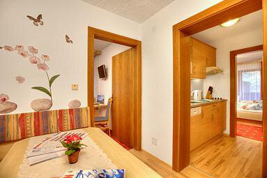 A bright room with wooden floors and modern furniture. The walls are decorated with floral motifs and there is a small kitchenette. - Haus Weisskogelblick - Vent