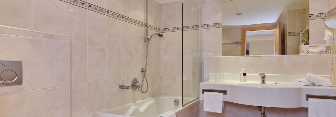A modern bathroom with a bathtub and a separate shower. The walls are light tiled and the floor has a red and white checkered pattern. - Hotel Vent - Vent
