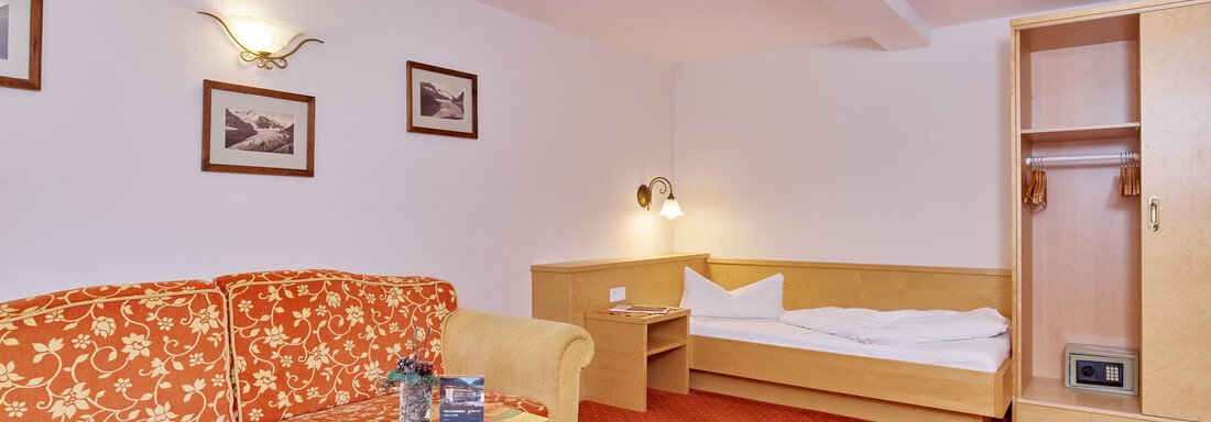 A cozy room with a red carpet and a sofa. There is a table, a wardrobe, and a single bed. - Hotel Vent - Vent