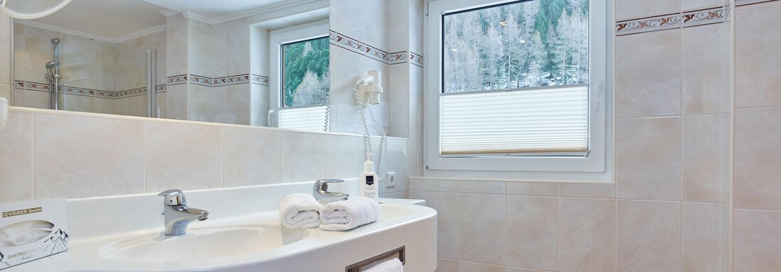 A modern bathroom with a white sink and a large mirror. The floor is designed with a red-and-white tile pattern, and there is a window with a view to the outside. - Hotel Vent - Vent