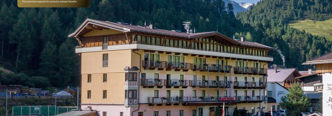 A hotel building in the mountains with several windows and balconies. In the foreground, vehicles are parked, and the surroundings are surrounded by green hills. - Hotel Vent - Vent