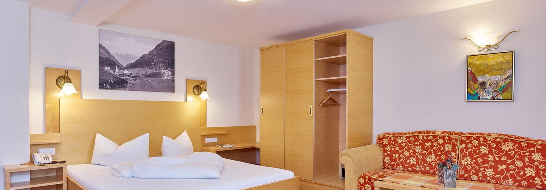 A modern hotel room with a double bed, a seating area, and a wardrobe. The walls are light, and there are decorative pictures. - Hotel Vent - Vent