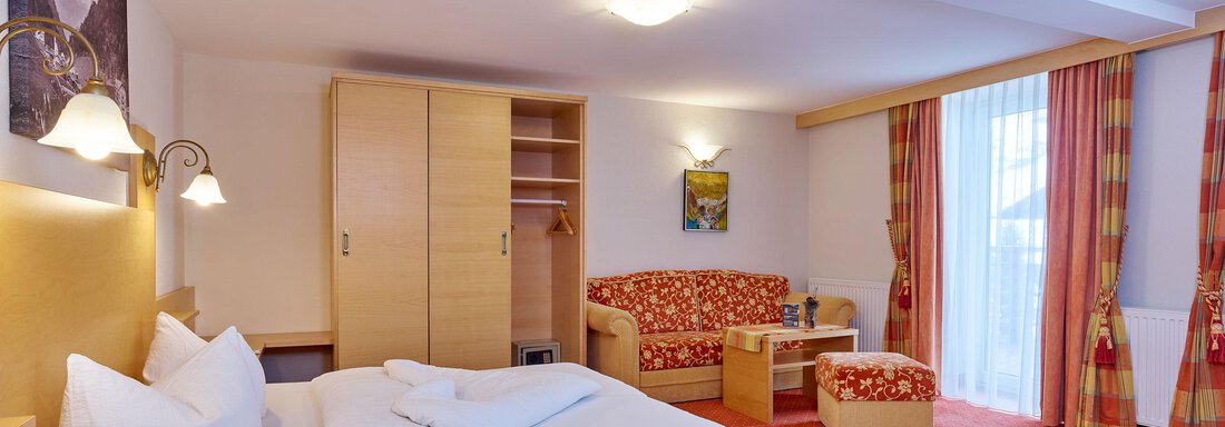 A cozy hotel room with a double bed, a sofa, and a large window. The decor is modern and friendly, with warm colors. - Hotel Vent - Vent