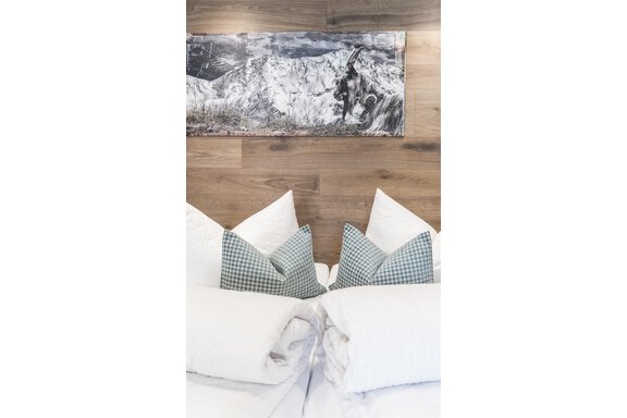 A cozy bedroom with white pillows and checkered decorative cushions. A picture of a mountain landscape hangs on the wall. - Garni Ötztal ROOMS & APARTS - Zwieselstein