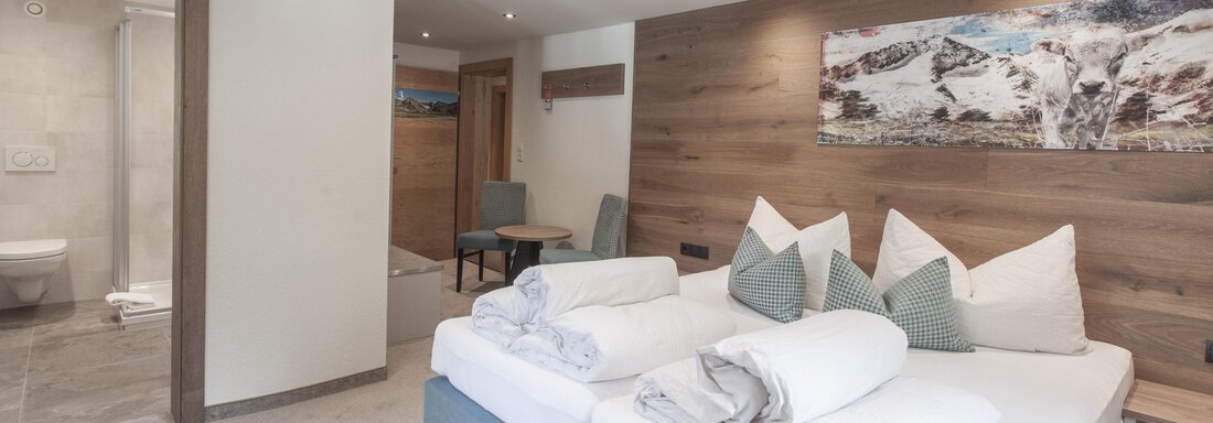 A modern bedroom with a large bed and cozy pillows. The walls are made of wood, and there is a window that lets in natural light. - Garni Ötztal ROOMS & APARTS - Zwieselstein