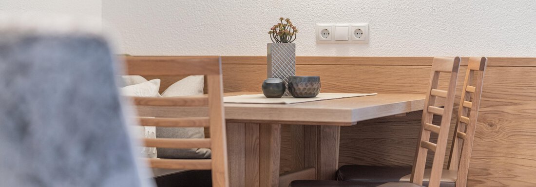 A cozy dining area with a wooden table and chairs. The table is decorated with plants and candles, the room has light walls and wooden details. - Garni Ötztal ROOMS & APARTS - Zwieselstein