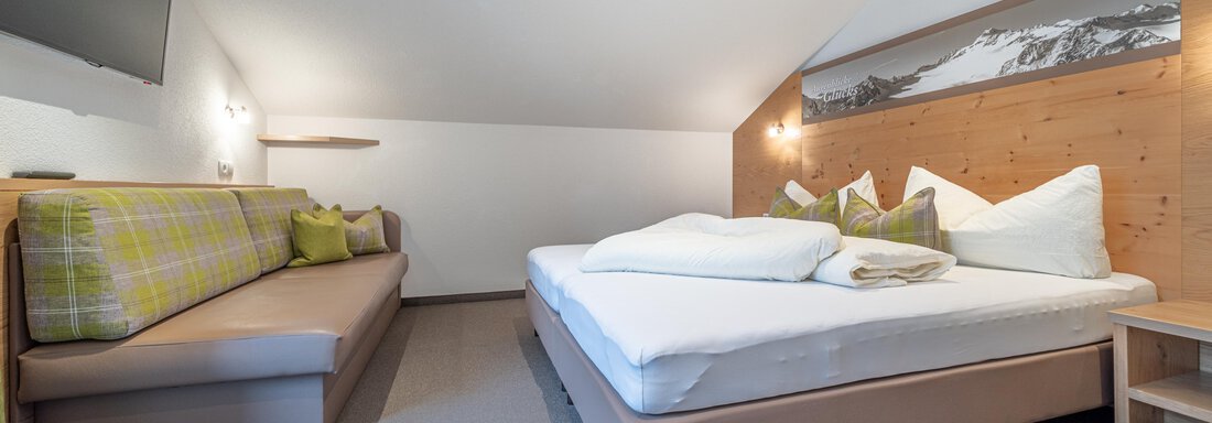 A cozy bedroom with a double bed and a comfortable couch. The walls are painted in neutral colors, creating a relaxed atmosphere. - Garni Ötztal ROOMS & APARTS - Zwieselstein