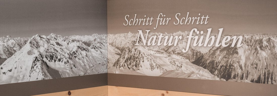 A mural depicts an impressive mountain landscape with snow-covered peaks. Below it is the inscription "Feeling nature step by step." - Garni Ötztal ROOMS & APARTS - Zwieselstein