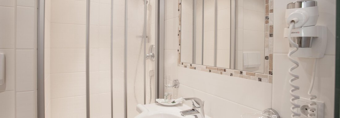A modern bathroom with a shower behind glass walls. The vanity is bright and clean with a large mirror. - Garni Ötztal ROOMS & APARTS - Zwieselstein