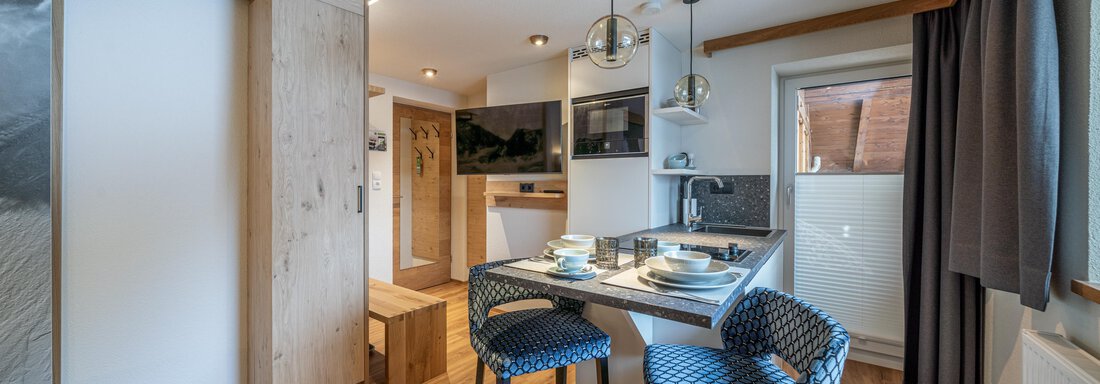 Studio | © Johannes Brunner, Michaela Jörg (CC C) A modern kitchen with wooden flooring and elegant bar stools. The room is bright and cheerful, perfect for cooking and relaxing. - Garni Ötztal ROOMS & APARTS - Zwieselstein