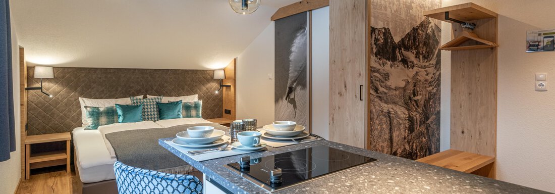 A modern room with a double bed and stylish decorations. The kitchen is open and well-equipped, ideal for a comfortable stay. - Garni Ötztal ROOMS & APARTS - Zwieselstein