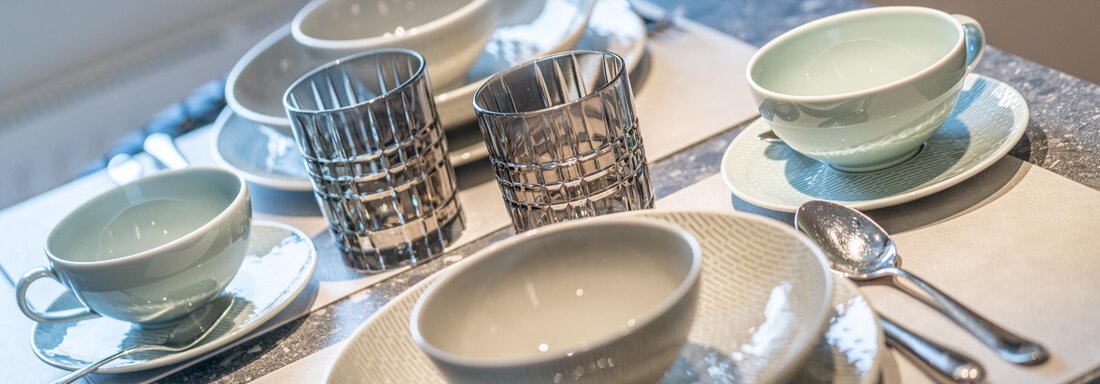 A beautifully set table with dishes in various colors. There are bowls, plates, and glasses with a modern design. - Garni Ötztal ROOMS & APARTS - Zwieselstein