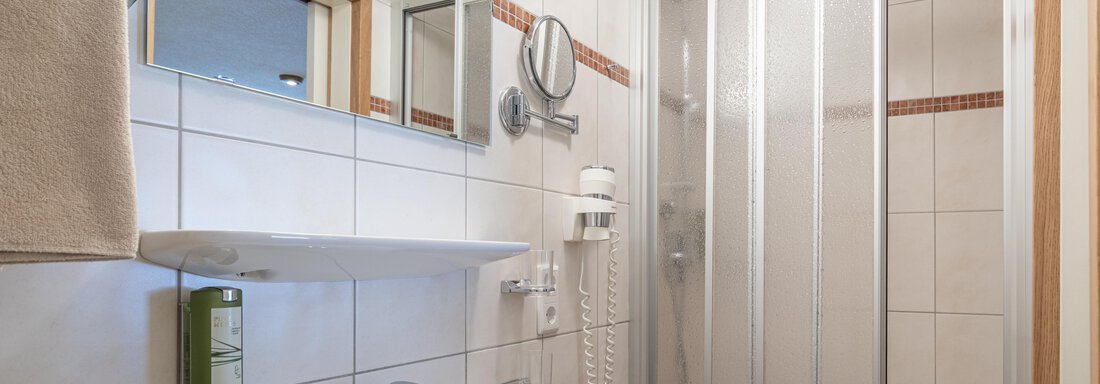 A modern bathroom with a shower cubicle and a sink. The walls are decorated with white tiles and a large mirror. - Garni Ötztal ROOMS & APARTS - Zwieselstein
