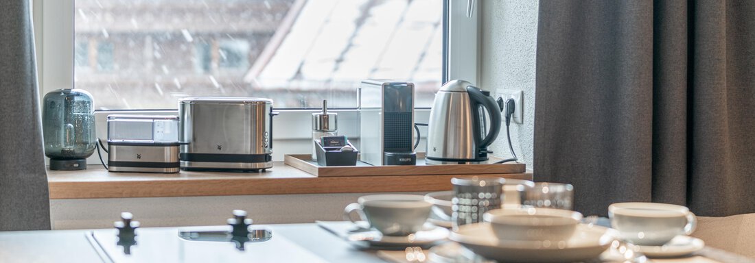 Modern kitchen with appliances such as toaster, kettle, and coffee machine. The table is set with dishes and cutlery. - Garni Ötztal ROOMS & APARTS - Zwieselstein