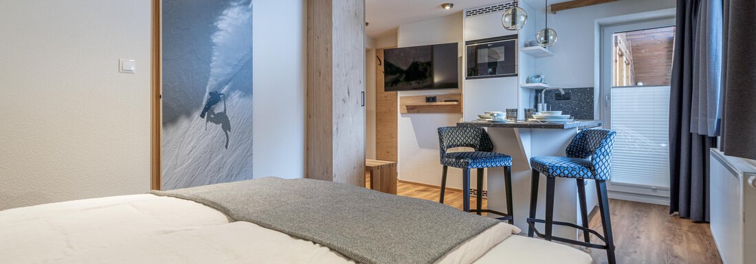 A modern room with a large bed and a well-equipped kitchenette. The room has wooden flooring and bright walls. - Garni Ötztal ROOMS & APARTS - Zwieselstein