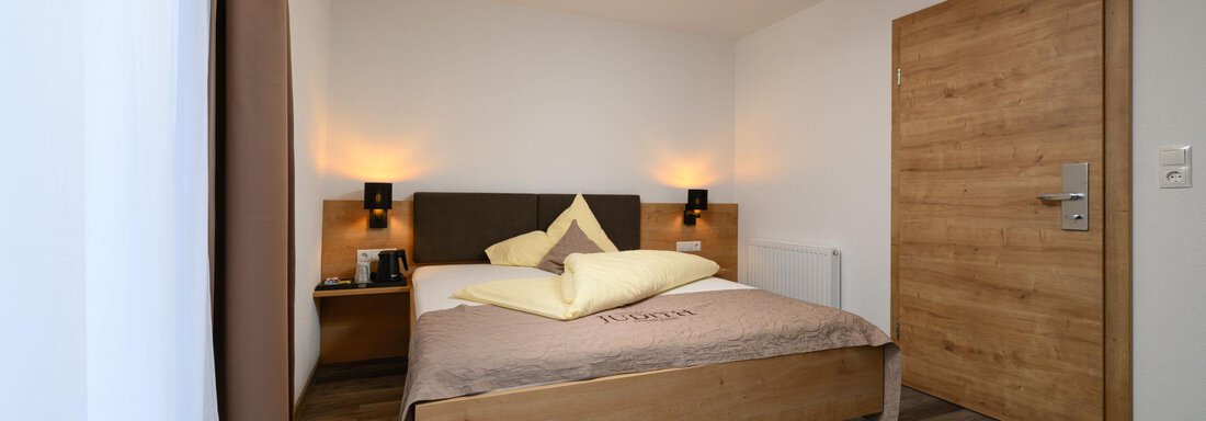 Einzelzimmer A cozy bedroom with a large bed and warm wooden design. The walls are light and there is soft lighting. - Gästehaus Judith - Zwieselstein