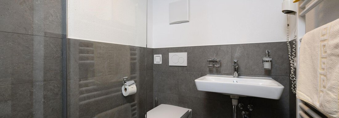 A modern bathroom with gray tiles and elegant fixtures. The atmosphere is simple and minimalist. - Gästehaus Judith - Zwieselstein