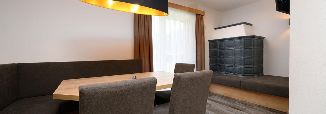 A modern living room with a cozy seating area and a large table. The walls are bright, and a big television is mounted. - Gästehaus Judith - Zwieselstein