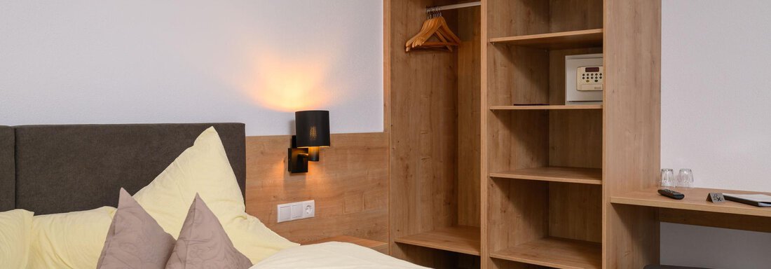 A modern bedroom with a large bed and yellow beddings. In the background, there is an open wardrobe and a small desk. - Gästehaus Judith - Zwieselstein