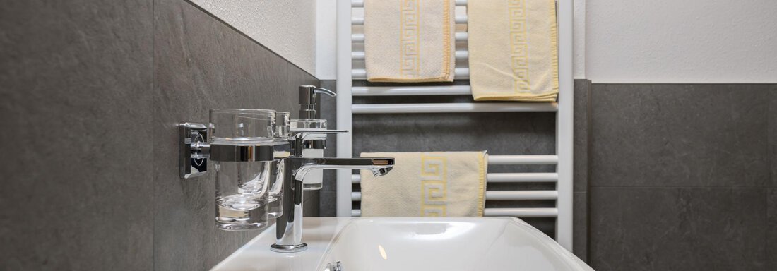 A modern bathroom with a white sink and a towel rack. On the towel rack, there are two yellow towels. - Gästehaus Judith - Zwieselstein
