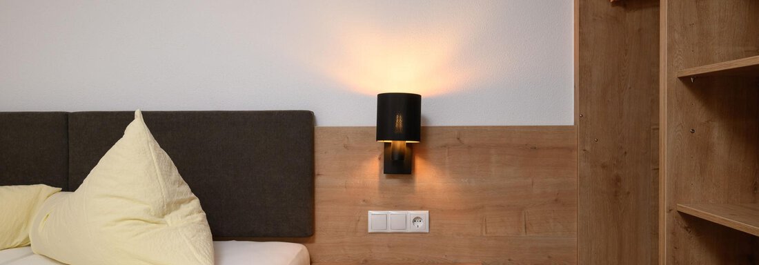 A modern bedroom with a wooden shelf and cozy lighting. The bed is styled with yellow pillows. - Gästehaus Judith - Zwieselstein