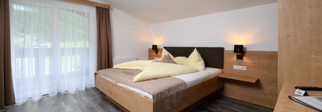 A modern bedroom with a double bed and wooden interior. Large windows provide plenty of daylight and a friendly atmosphere. - Gästehaus Judith - Zwieselstein