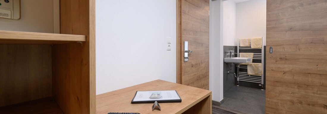 A modern room with wooden furniture and an elegant desk area. In the background, a bathroom can be seen. - Gästehaus Judith - Zwieselstein
