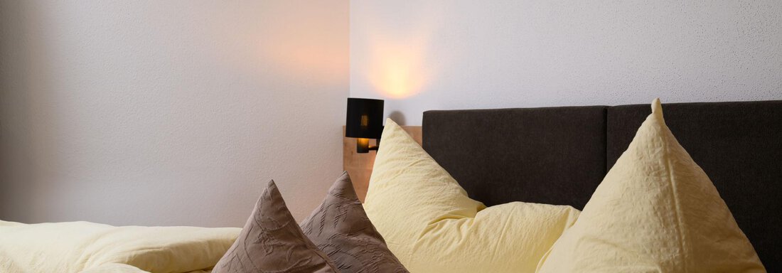 A cozy bedroom with a large bed and soft pillows. The calming atmosphere is enhanced by soft light and simple furnishings. - Gästehaus Judith - Zwieselstein