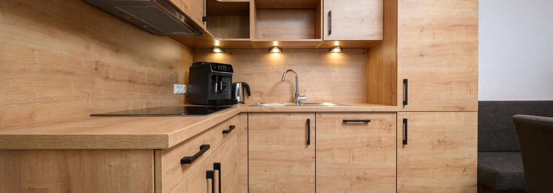 A modern kitchen with wooden cabinets and a bright countertop. The amenities include a kettle and a sink, surrounded by plenty of storage space. - Gästehaus Judith - Zwieselstein