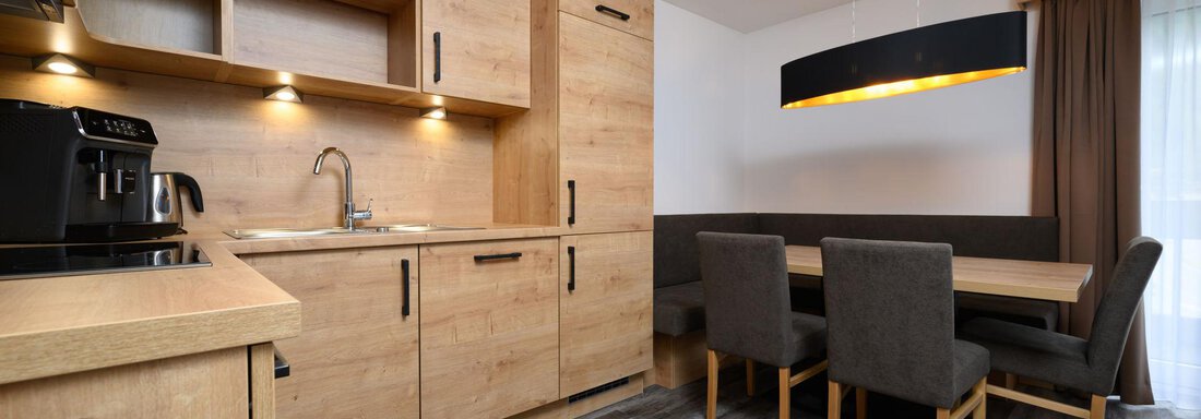 A modern kitchen with wooden cabinets and a bright, inviting atmosphere. The dining table with chairs complements the space. - Gästehaus Judith - Zwieselstein
