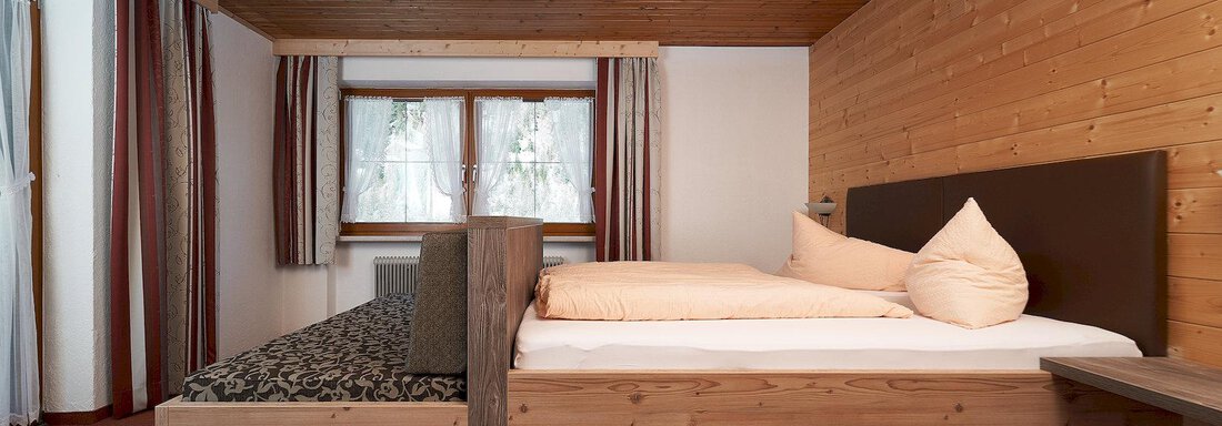 A cozy bedroom with wooden paneling and two beds. Large windows provide plenty of daylight. - Gästehaus Judith - Zwieselstein