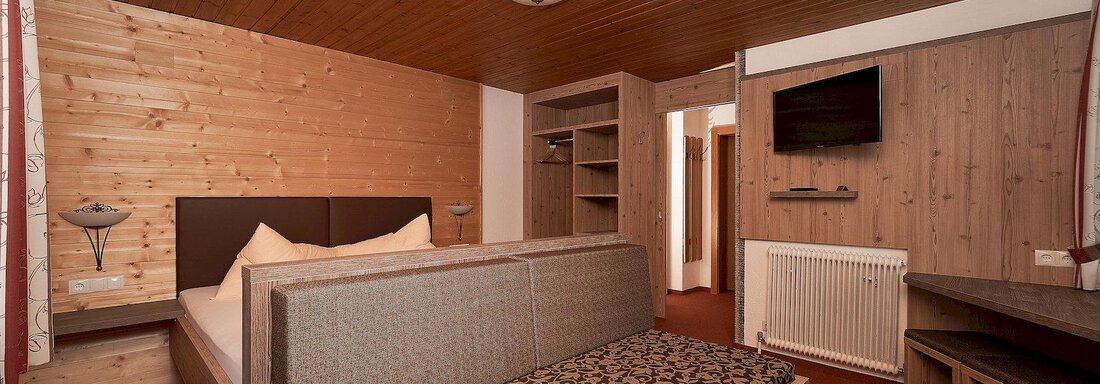 A cozy room with wood paneling and a modern design. It is equipped with a bed, a sofa, and a television. - Gästehaus Judith - Zwieselstein