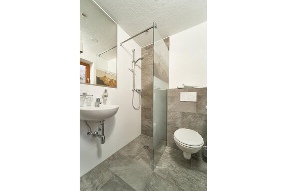 A modern bathroom with a glass shower and a sink. The walls are in neutral tones and the tiles are elegantly designed. - Gästehaus Judith - Zwieselstein
