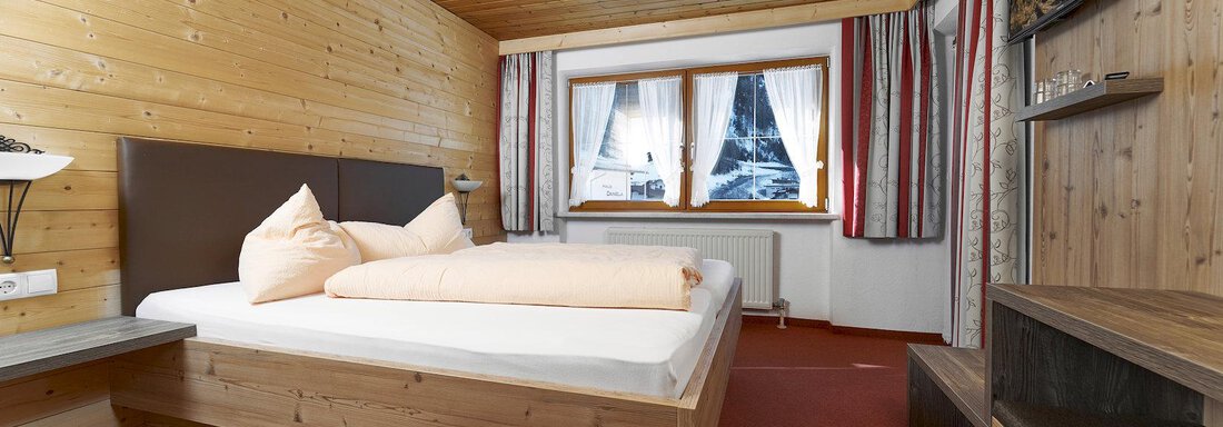 A cozy bedroom with wooden paneling and a comfortable bed. The windows provide daylight and offer a beautiful view. - Gästehaus Judith - Zwieselstein