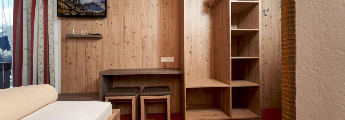 A cozy room with wood paneling and a double bed. There is a small table with chairs and a wardrobe for storage. - Gästehaus Judith - Zwieselstein