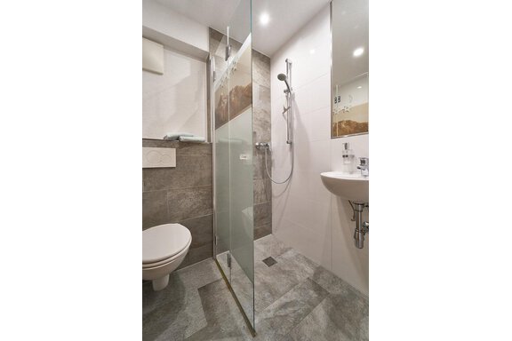 A modern bathroom with a clear shower partition and a sink. The walls are in neutral colors, and the floor is made of gray tiles. - Gästehaus Judith - Zwieselstein