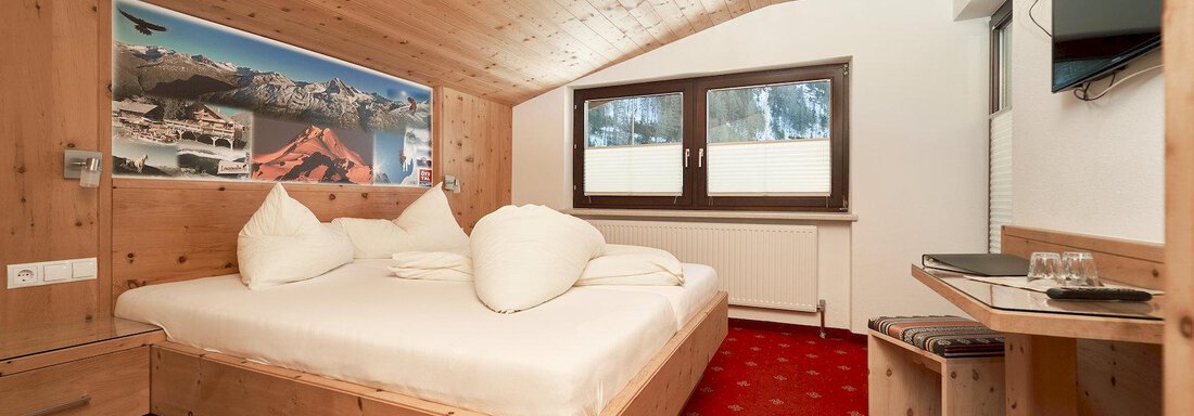 A cozy room with wooden paneling and a double bed. There is a small table and a television on the wall. - Gästehaus Judith - Zwieselstein