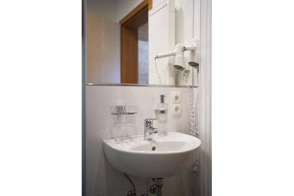 A modern bathroom with a first sink and a hairdryer. The walls are in light colors, and there is a clean, tidy atmosphere. - Gästehaus Judith - Zwieselstein