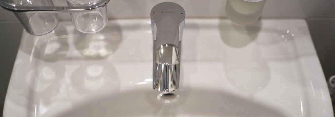 A modern sink with a shiny faucet. In the background, two glasses and a soap dispenser can be seen. - Gästehaus Judith - Zwieselstein