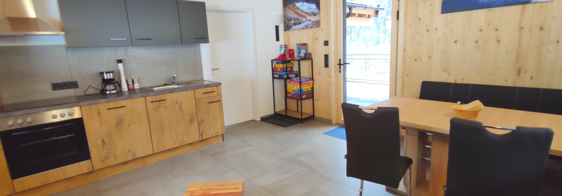 A modern kitchen with wooden shelves and a cozy dining area. The room has large windows and plenty of natural light. - Haus Fortuna - Zwieselstein