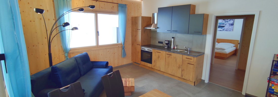 A modern apartment with wooden paneling and large windows. It has a kitchenette, a sofa, and a dining area. - Haus Fortuna - Zwieselstein