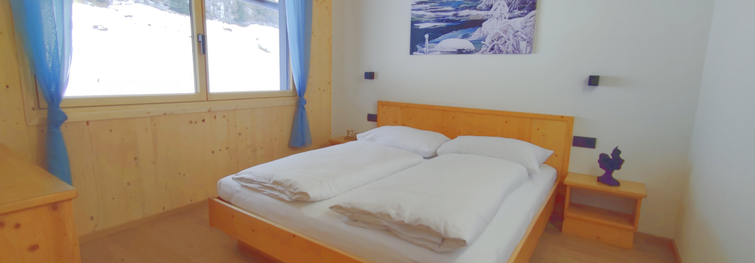 A cozy bedroom with a wooden bed and white bedding. Through the window, you can see a snowy landscape. - Haus Fortuna - Zwieselstein