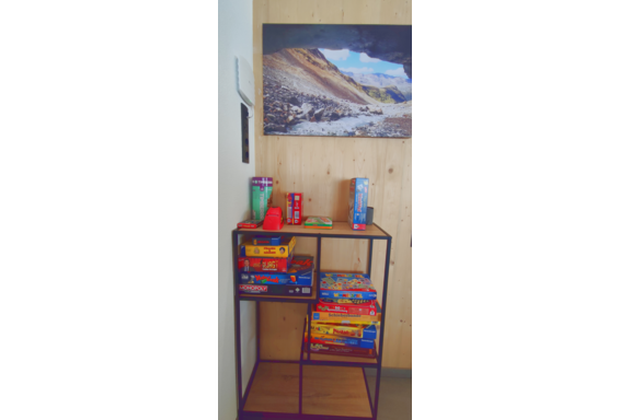 A shelf with various board games and a red toy. In the background, there is a picture of a mountainous landscape. - Haus Fortuna - Zwieselstein