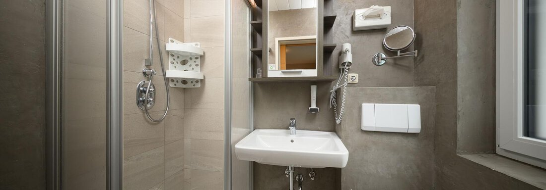 A modern bathroom with a shower, a sink, and a toilet. The walls are in a neutral color tone and there are practical shelves. - Haus Sonnschein - Zwieselstein