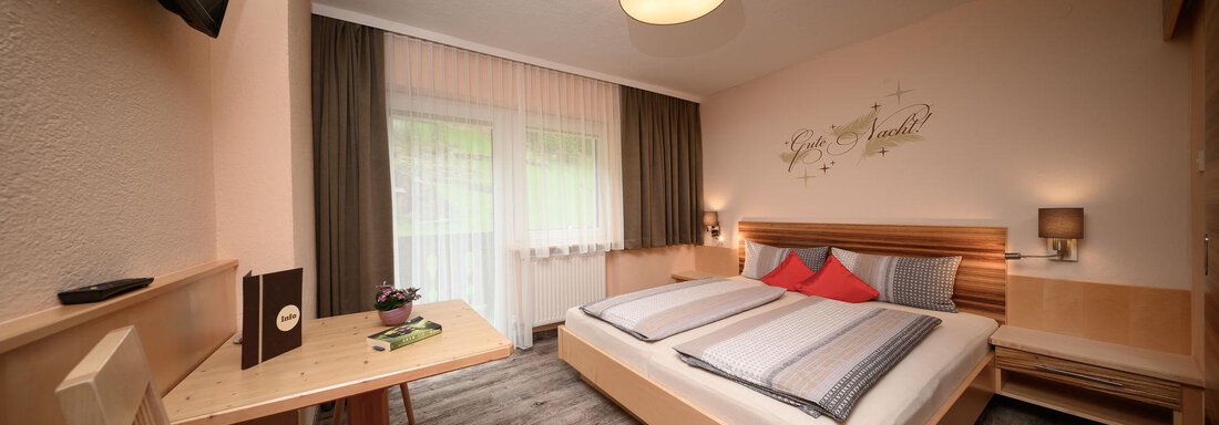 A modern bedroom with a large bed and red pillows. The room has wooden furniture and large windows that let in a lot of daylight. - Haus Sonnschein - Zwieselstein